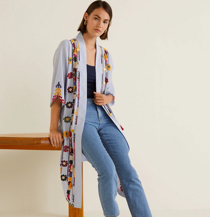 picture of a woman leaned on a table wearing jeans, shirt and a kaftan