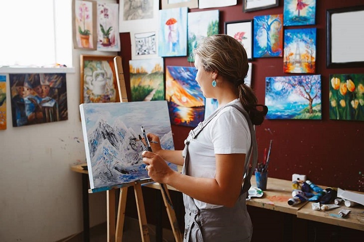 picture of a woman painting in a room with paintings on the wall 