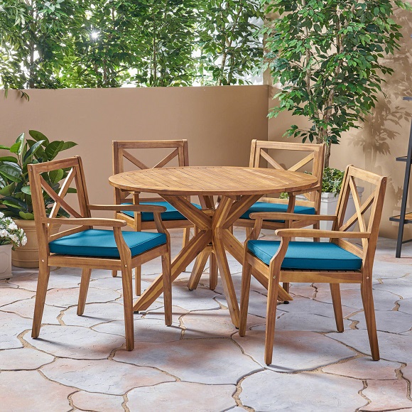Four teak armchairs with blue seating cushions and a teak table
