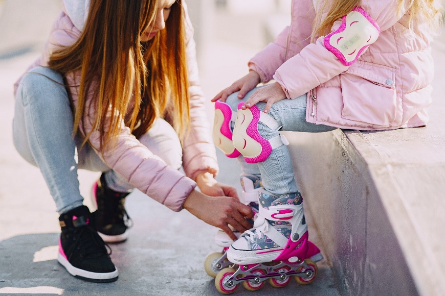 Мother fastens the girl's roller skates
