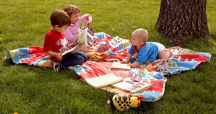 three kids reading outside on the grass