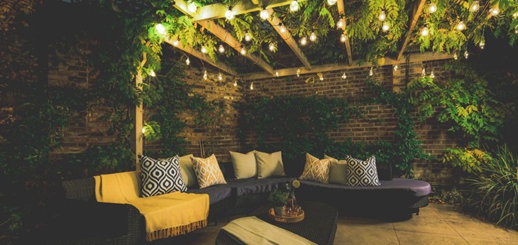 a garden couch placed under a roof decorated with light bulbs and greenery 