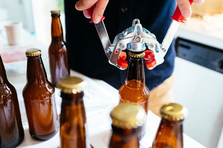 Some guy closing glass beer bottles with a tool